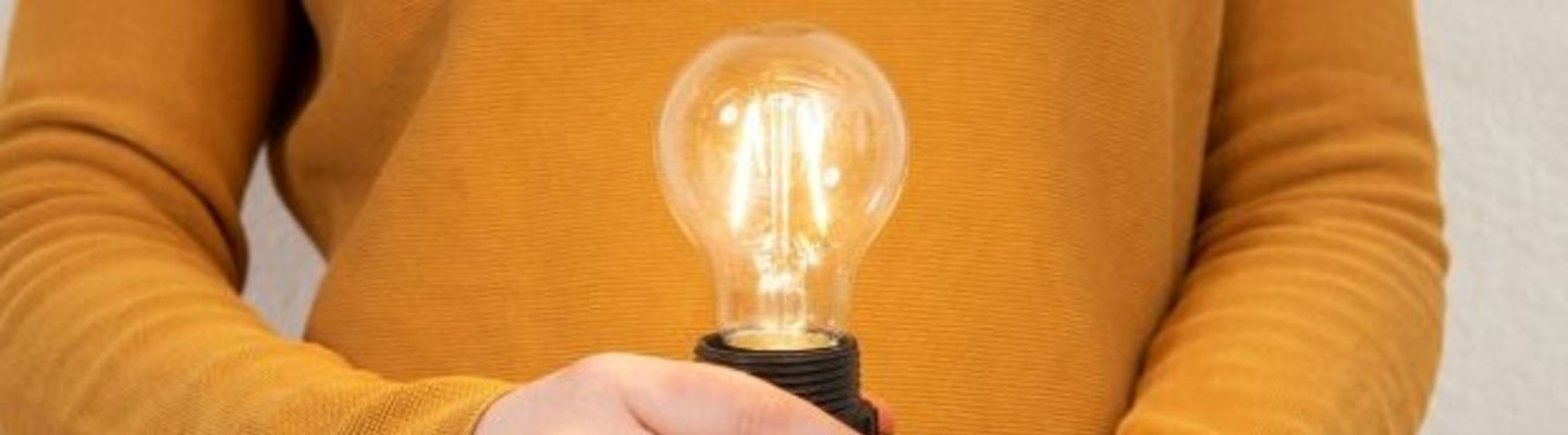 Hand hält leuchtendes LED Leutmittel vor Oberkörper